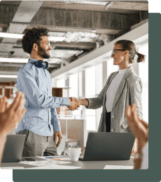 Young male worker who is smiling, stands up to shake the hand of a female co-worker